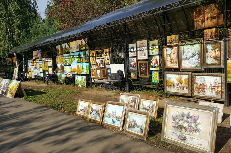 A full shot of paintings on display by the side of the road in a waiting shade.