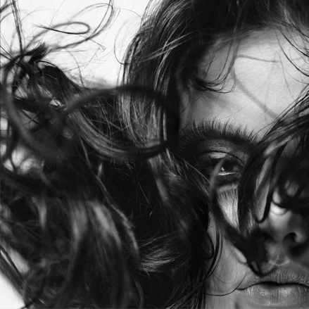 A close-up shot of a woman with her hair covering her face. A photograph of Christopher MiCaud in black and white.